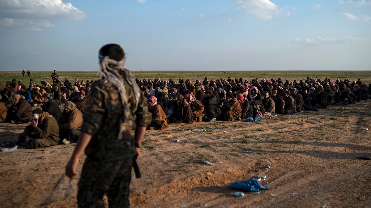US-backed Syrian Democratic Forces (SDF) fighters stand guard next to men waiting to be screened after being evacuated out of the last territory held by Islamic State group militants, near Baghouz, eastern Syria.