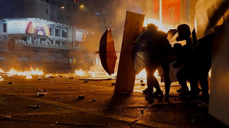 Hong Kong protesters shelter behind a thin barrier – and umbrellas – as police fire tear gas and encircle a group of demonstrators.&nbsp;