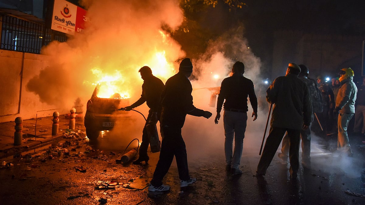 Police personnel attempt to douse a burning vehicle torched allegedly by protestors during a rally against the Citizenship Amendment Act (CAA), in New Delhi.