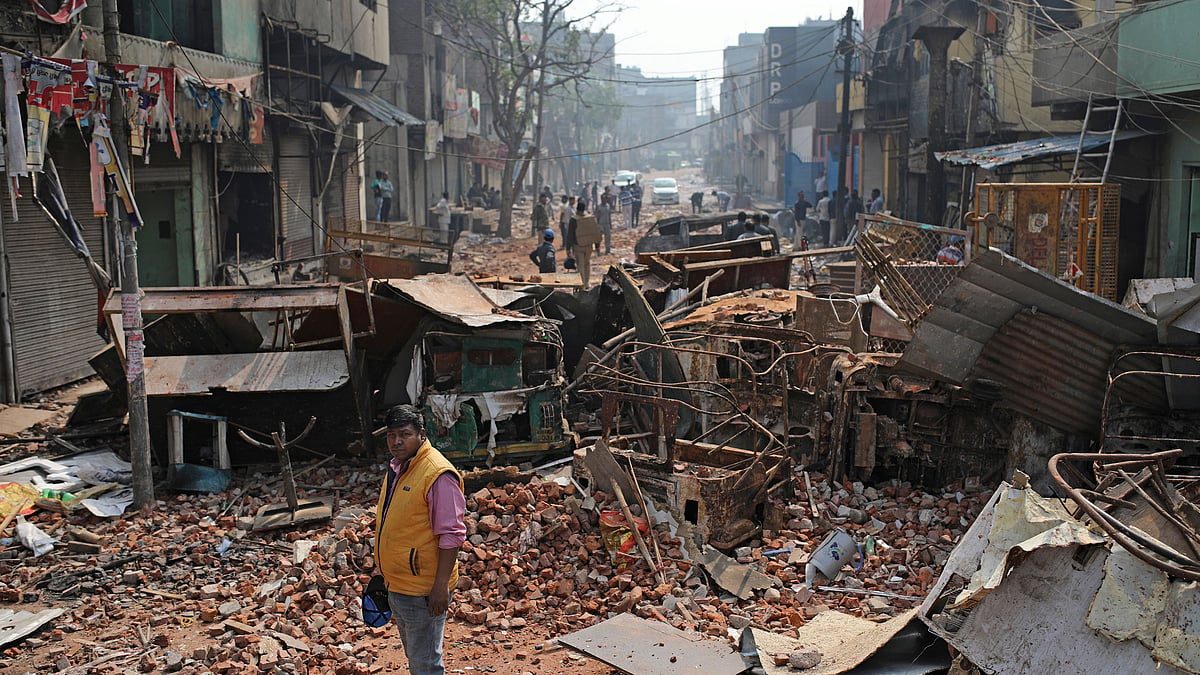 A Delhi municipal worker stands next to the remains of vehicles, and other materials on a street vandalised in violence in New Delhi, on 27 February.