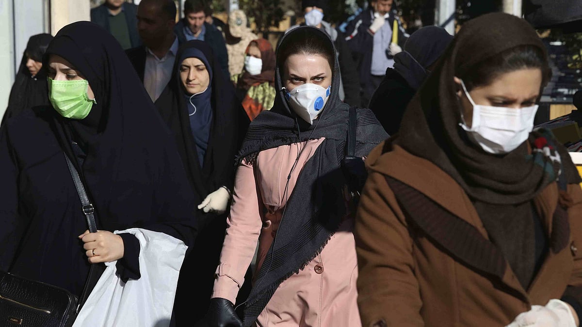 People wearing face masks walk on a sidewalk in Tehran, Iran.