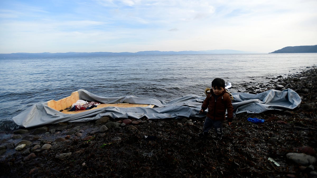 A boy stands next to a dinghy at the village of Skala Sikaminias, on the Greek island of Lesbos, after crossing with other migrants the Aegean sea from Turkey, Sunday, 1 March. 