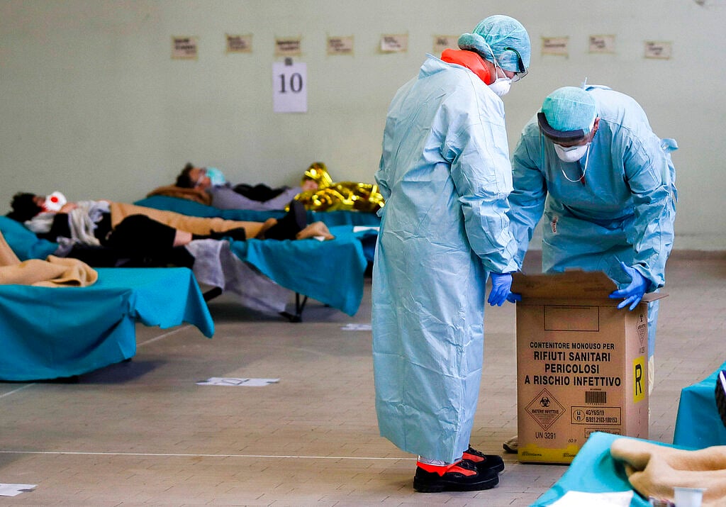 Paramedics carry an hazardous medical waste box as patients lie on camping beds, in one of the emergency structures that were set up to ease procedures in northern Italy, March 12, 2020.