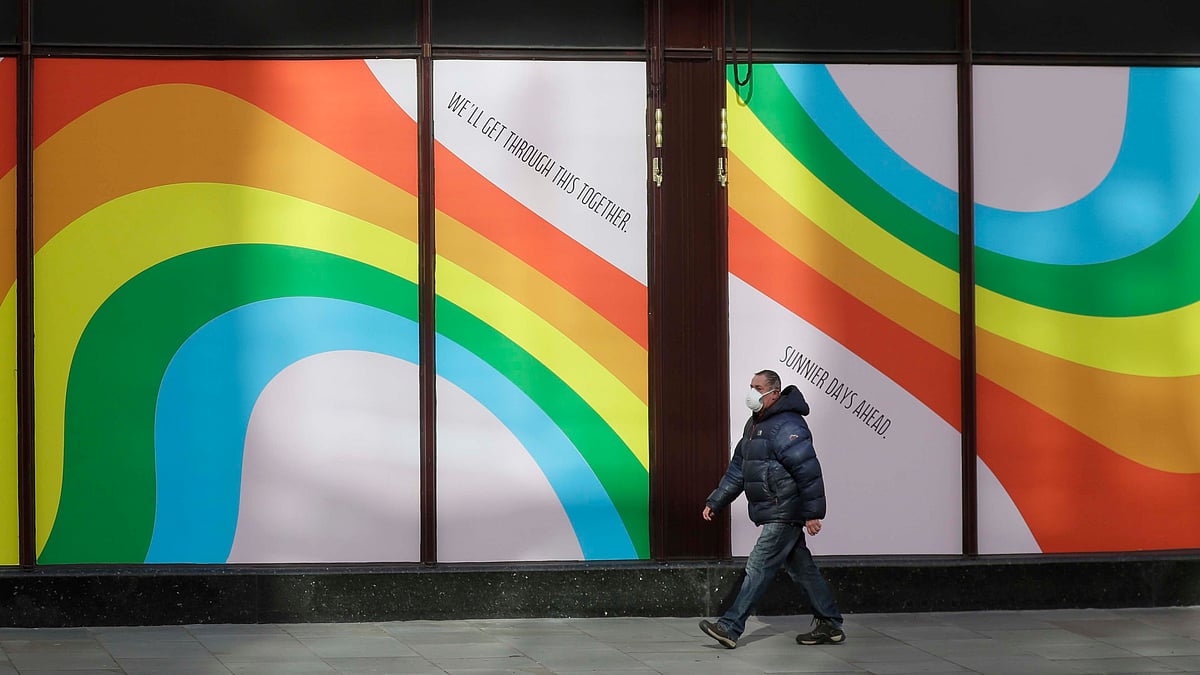 A man wearing a face mask to protect against catching the coronavirus walks past a window display of rainbows in the windows of the famous London department store Harrods in London, Tuesday, 31 March, 2020. 