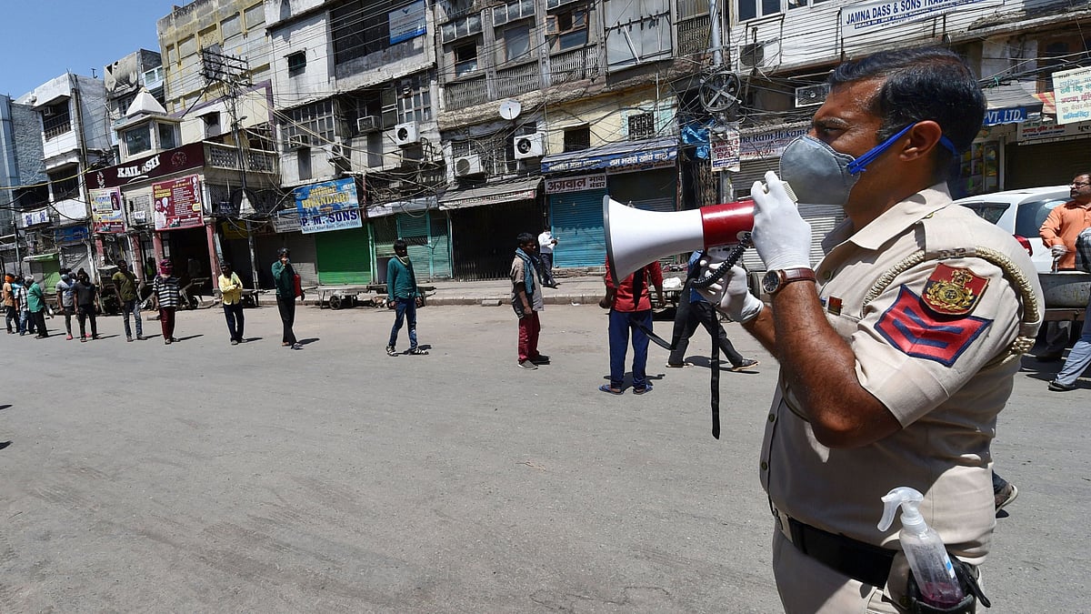 A policeman with a hand sanitiser in his holster makes announcements using a loudspeaker as homeless people stand in a queue to receive food, during the nationwide lockdown to curb the spread of coronavirus, at Khari Baoli in New Delhi, Wednesday, April 8, 2020.