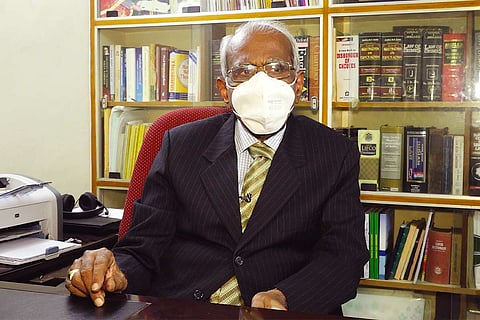 Justice AK Rajan sits at his desk with a bookshelf of books behind him 