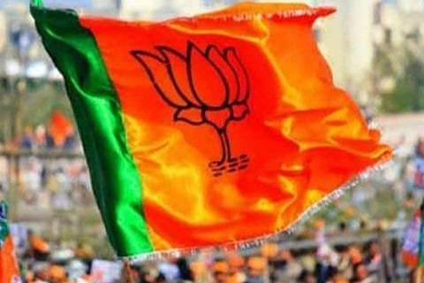 BJP flag which is saffron and green with a lotus in the middle flies and in the background party worker 