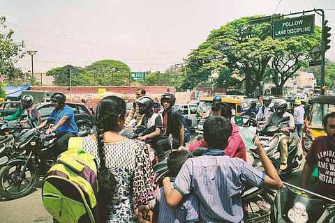 A woman accompanies two school students as they wait to cross a traffic-packed road in Bengaluru. 