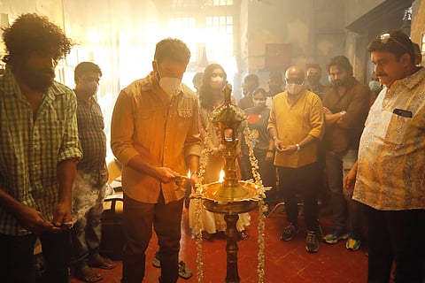 Prithviraj wearing a mask and lighting lamp for pooja with crew watching 