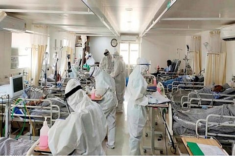 COVID-19 patients at a hospital with healthcare workers in PPE suits standing nearby