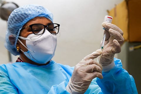 A woman health worker wearing PPE and a mask and gloves holds a vial of COVID-19 vaccine 