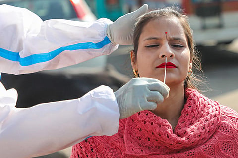 A health worker in a PPE suit collecting nasal swab sample from a woman in a red sweater for coronavirus test