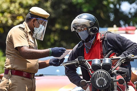 Policeman in gloves, mask and face shield checking the documents of a motorist who is sitting on a bike, wearing a helmet and mask