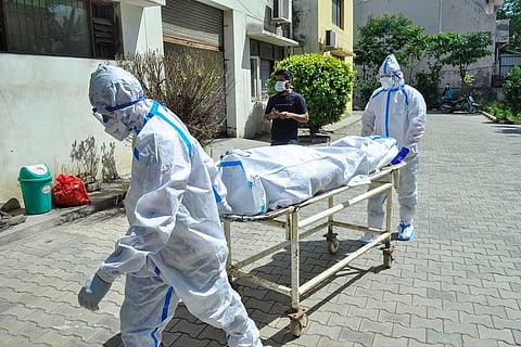 India COVID deaths: Two health workers wheeling out a body of a COVID victim on a stretcher