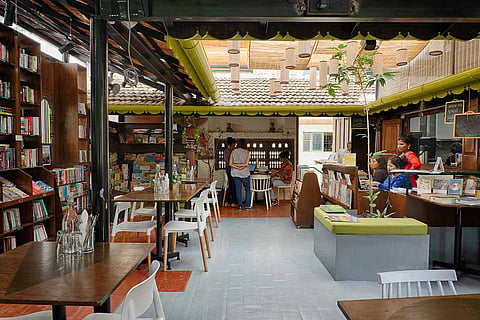 Interiors of a bookstore and cafe. Shelves of books on one side, with tables next to it. 