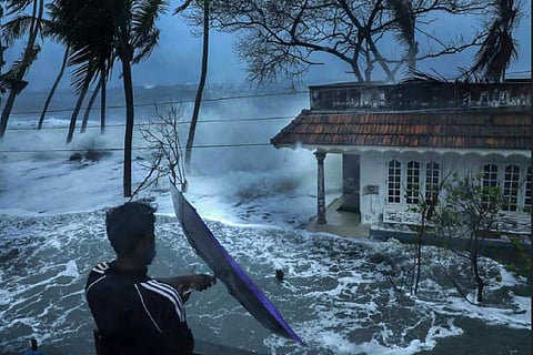 Man standing in front of a house hit by waves during coastal erosion