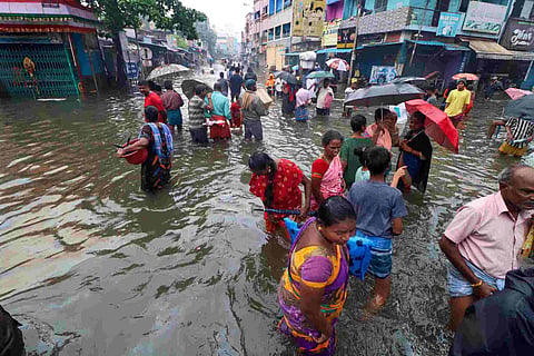 People walking in a submerged street in Chennai with some holding umbrellas
