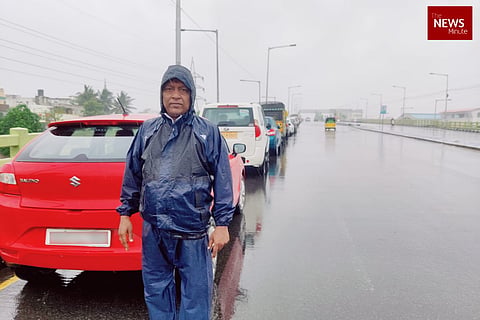 A man standing in front of his car in a blue raincoat on a flyover as heavy rains lash Chennai
