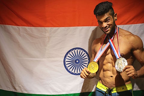Chennai bodybuilder Manikandan posing with his medals behind Indian flag. 