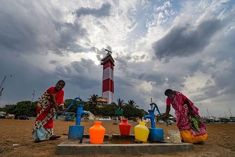 A group of women pumping water in the pump before the light house as the clouds are getting darker