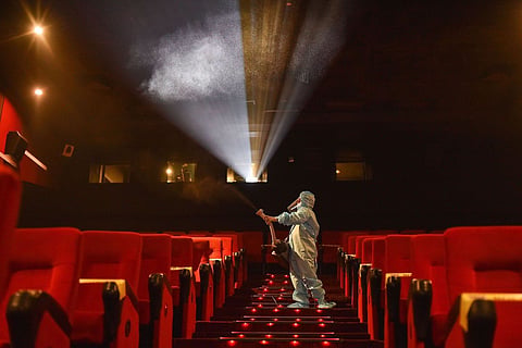 A theatre staff member in a PPE kit disinfecting a cinema hall