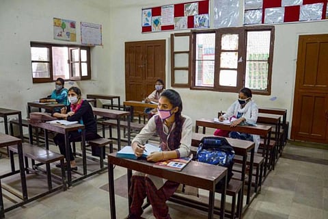 Five students sitting far apart on wooden benches in a classroom