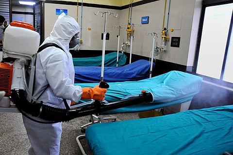 Man wearing a PPE kit spraying disinfectant in a hospital ward