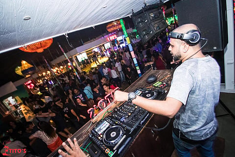 A DJ next to his console at Club Titos as the crowd before him dances away 