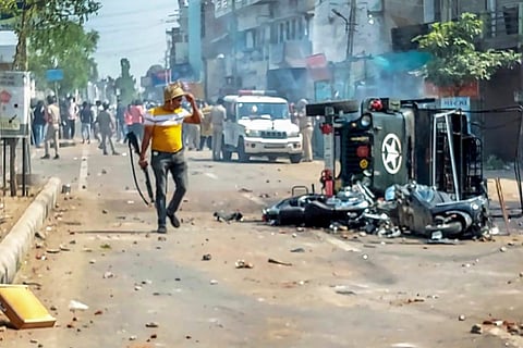 Himmatnagar: A policeman near a burnt vehicle as police try to control the situation after a communal clash during the Ram Navami procession