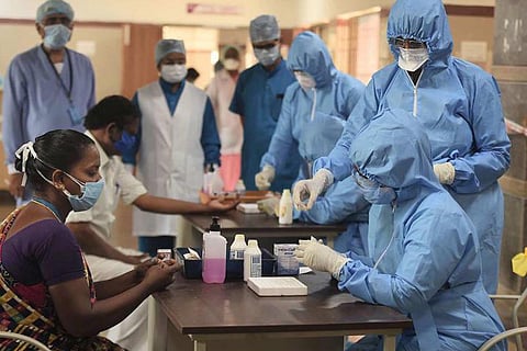 A woman sitting at a table while consulting with healthcare workers in blue PPE suits