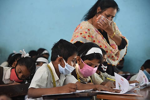A teacher is helping two students with masks 