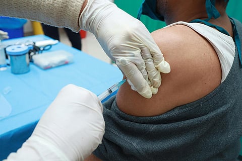 gloved hands inject covid-19 vaccine into the arm of a man, who has his t-shirt pulled down at the shoulder