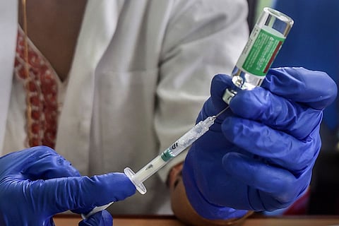 A medic holding a syringe and the vaccine bottle, preparing to administer the dose of COVID-19 vaccine to a beneficiary