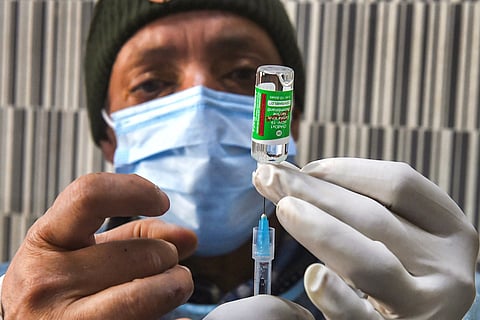 A medic wearing a mask holds up a vial containing dose of Covishield vaccine and a syringe
