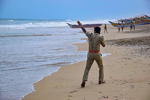A. police officer raises his left hand asking people to evacuate along the beach 
