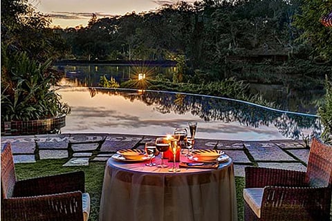 Two dining tables set out near a river as the sun sets