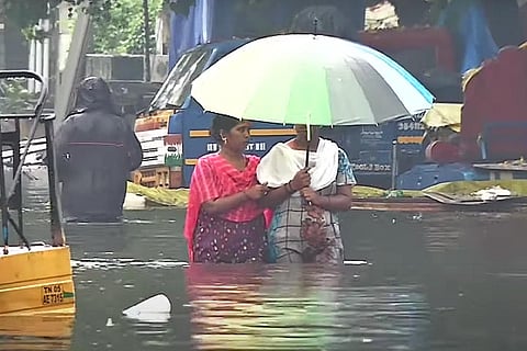 Two women walking through waist-deep water holding up an umbrella