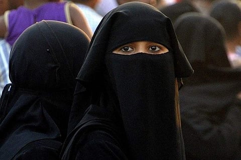 A burqa-wearing woman staring into the camera, surrounded by two other women in burqa