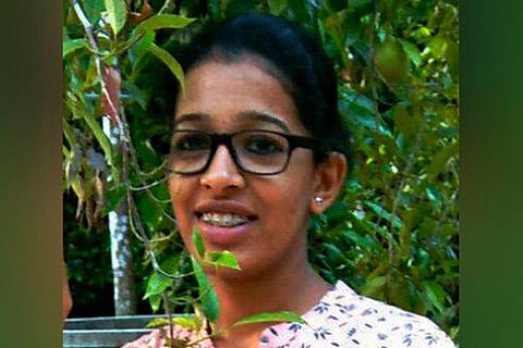 Jesna Maria James, a Bcom student from Kerala poses for the camera, behind her are shrubs and she is wearing a white shirt