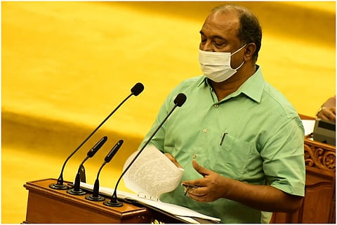Kerala Finance Minister KN Balagopal, in a light green shirt, wearing white mask, facing mike. 