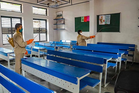 Healthcare workers sanitising a school classroom with blue and white benches