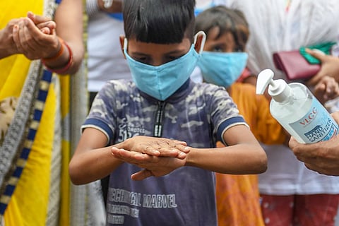 A small boy in mask sanitising his hands