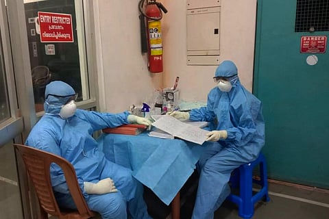 Two health workers in blue PPE suits sitting down in a hospital