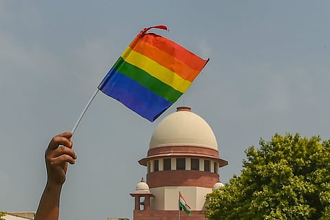 A person holding up a Pride flag in front of the Supreme Court of India