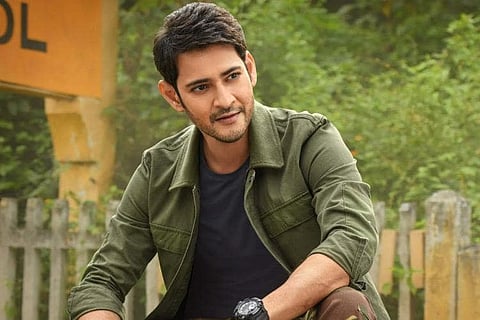 Mahesh Babu is seen wearing a blue tee and olive green jacket in the image. 
