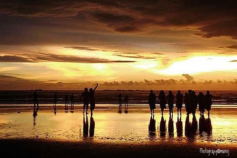 Silhouettes of people standing at a beach in Mangaluru at sunset