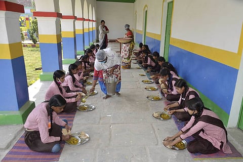Children sit on the floor in their school corridor to eat a mid-day meal