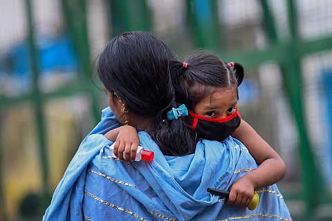A representative image of a woman carrying her child who is seen wearing a mask