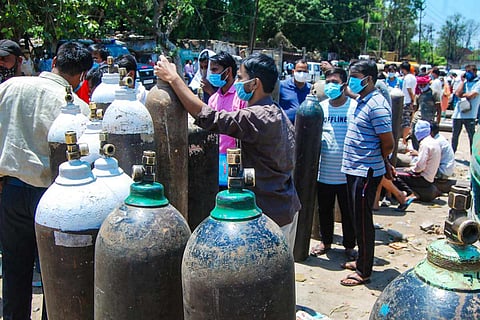 People stand near oxygen cylinders as demand for the gas rises due to a spike in coronavirus cases