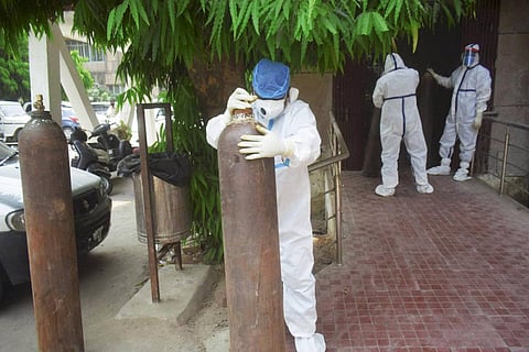 A health worker dressed in PPE standing and holding up an oxygen cylinder 